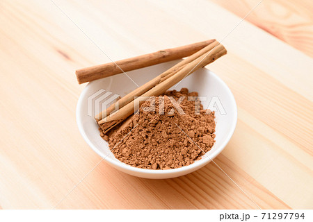 木目テーブルにある皿の上のシナモンスティックとシナモンパウダーの写真素材