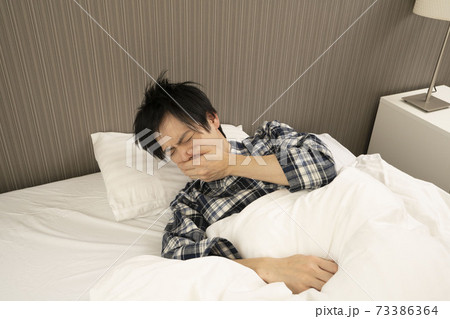 ベッドルームにてパジャマ姿でくしゃみをする男性