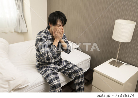 ベッドルームにてパジャマ姿でくしゃみをする男性