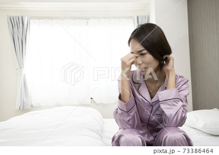 病気で寝込んでいる女性/体調の悪い女性/ベットに寝ている美しい女性/ベッドに座っている美人